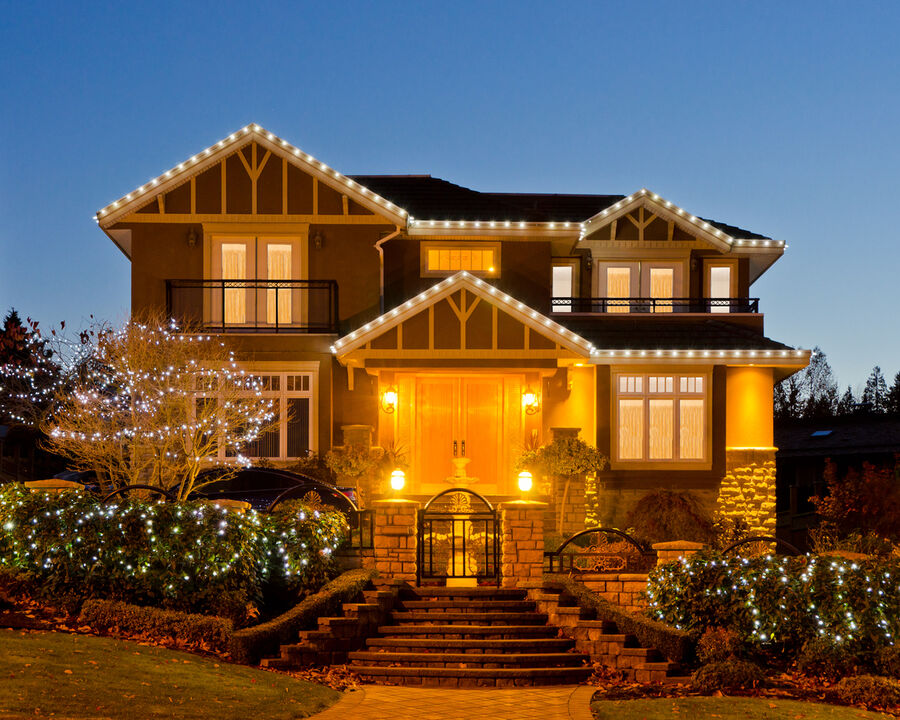Two-story house with outdoor LED lights along roofline, shrubs, and entryway at dusk