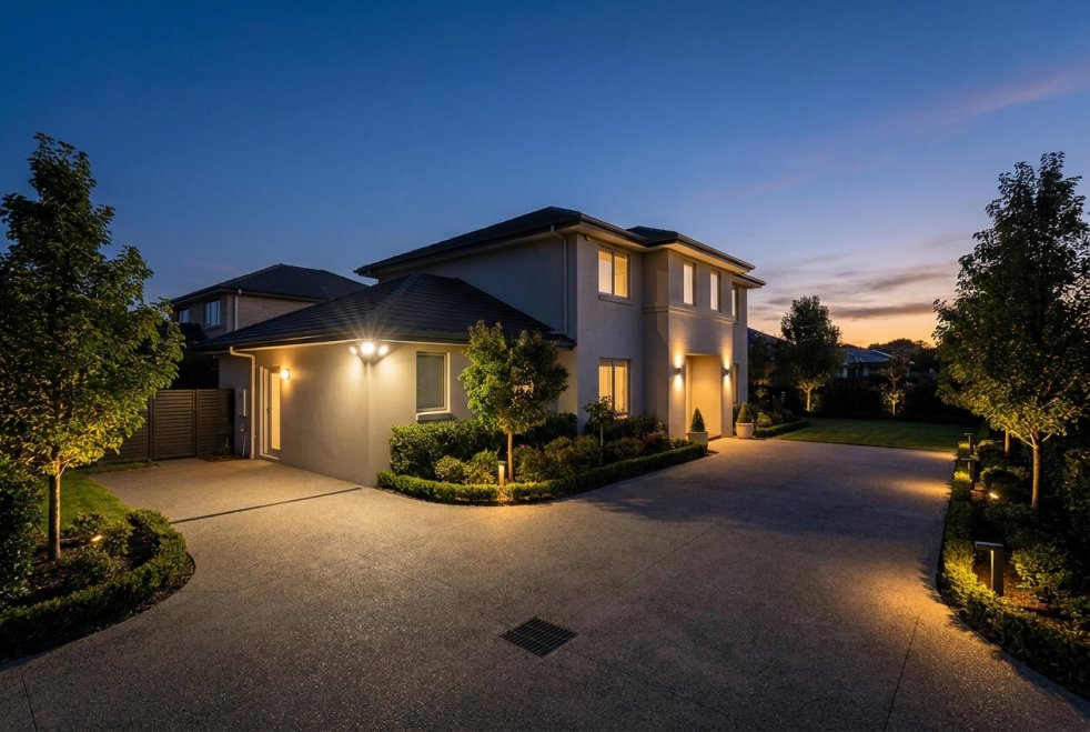 Modern home exterior with security lighting illuminating driveway and landscaped yard at dusk